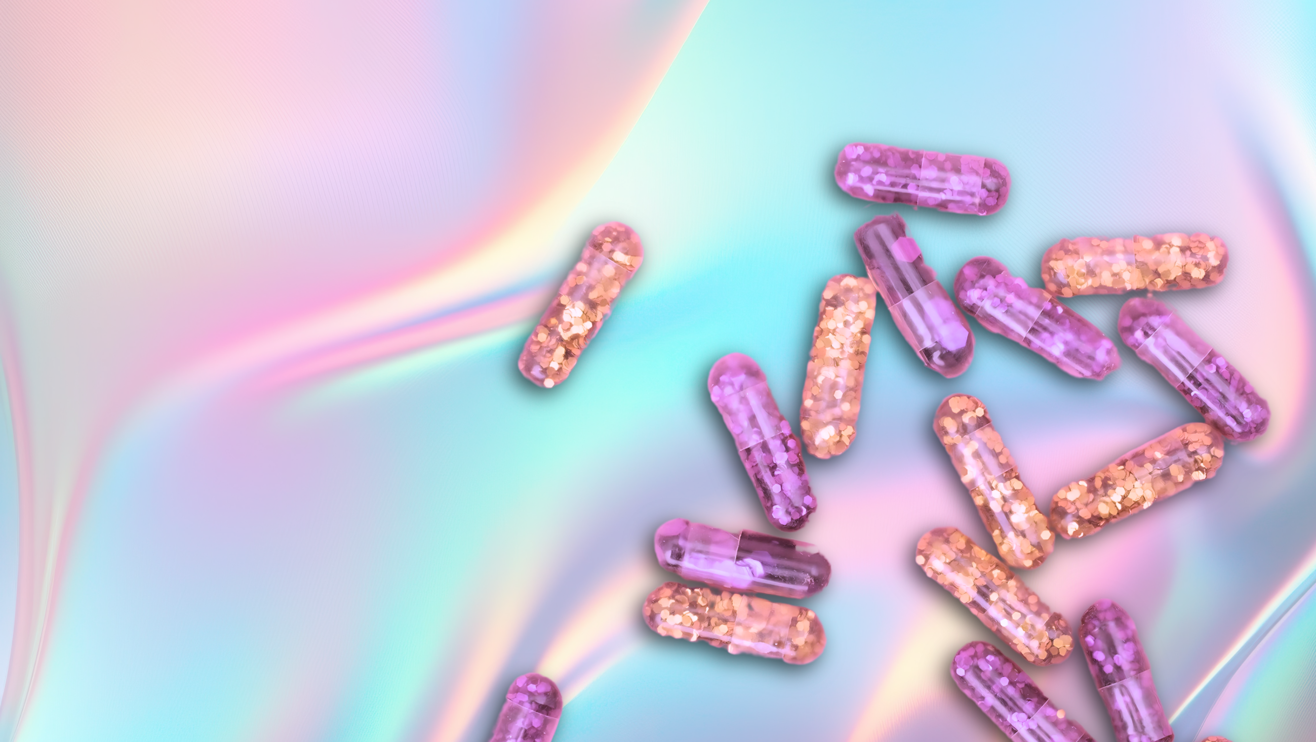 pastel pinks and blues in the background and pills filled with pink and orange glitter at the forefront